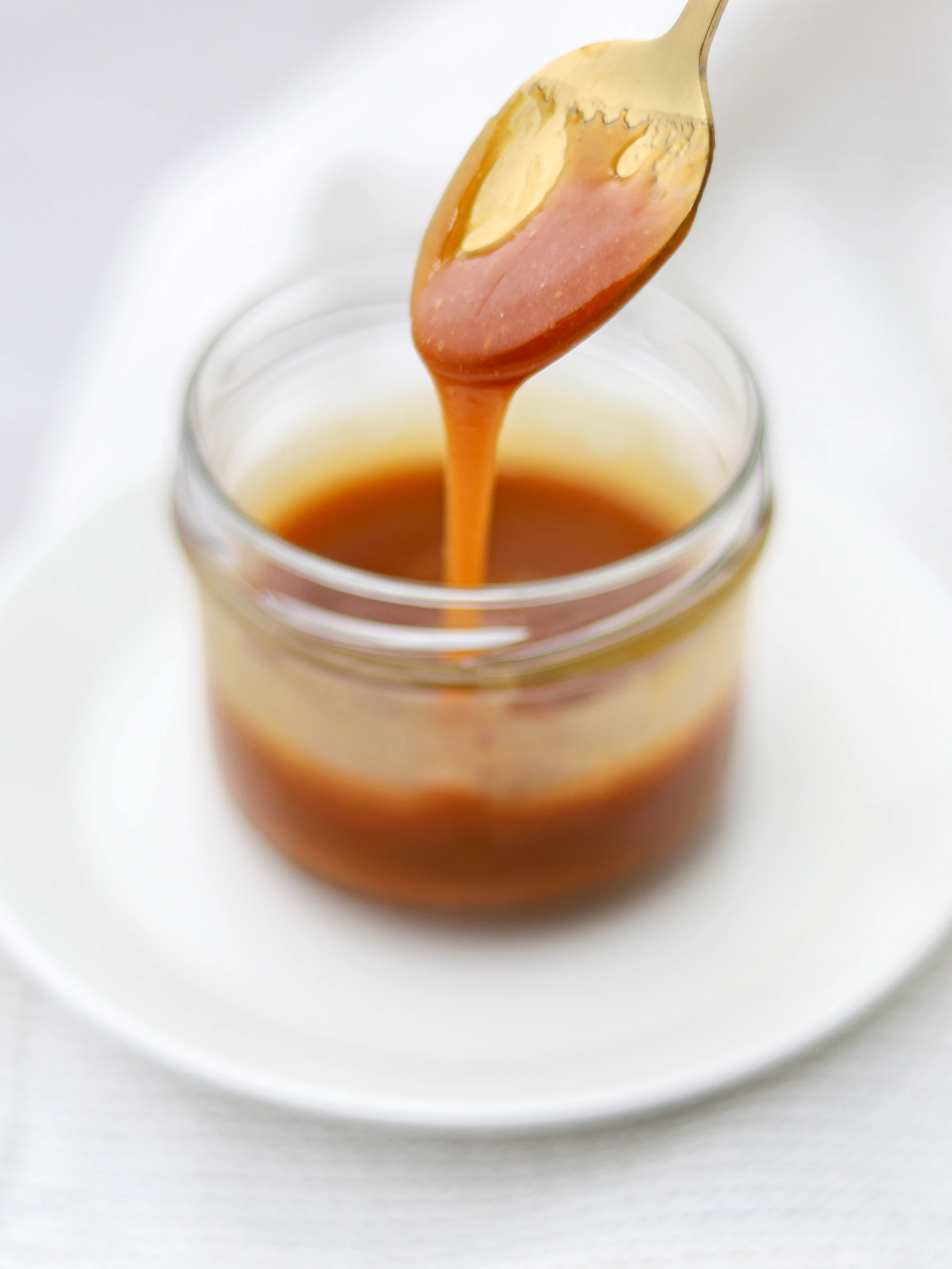 Honey dripping from a spoon into a glass jar