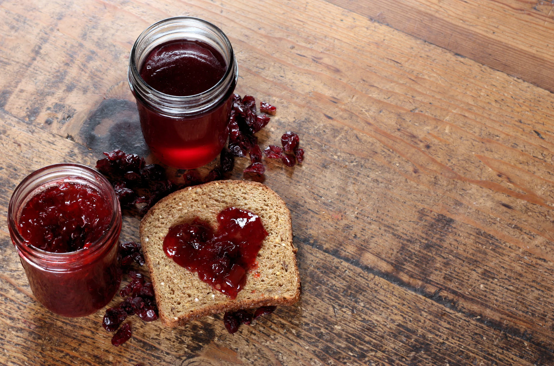 Two jars of jam beside toast on a wooden table